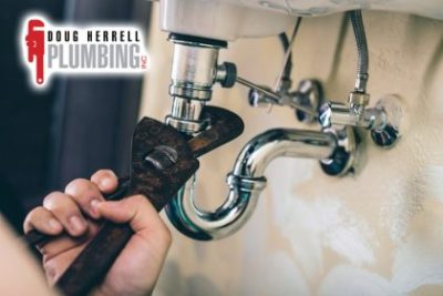 someone fixing a leak with a wrench under sink